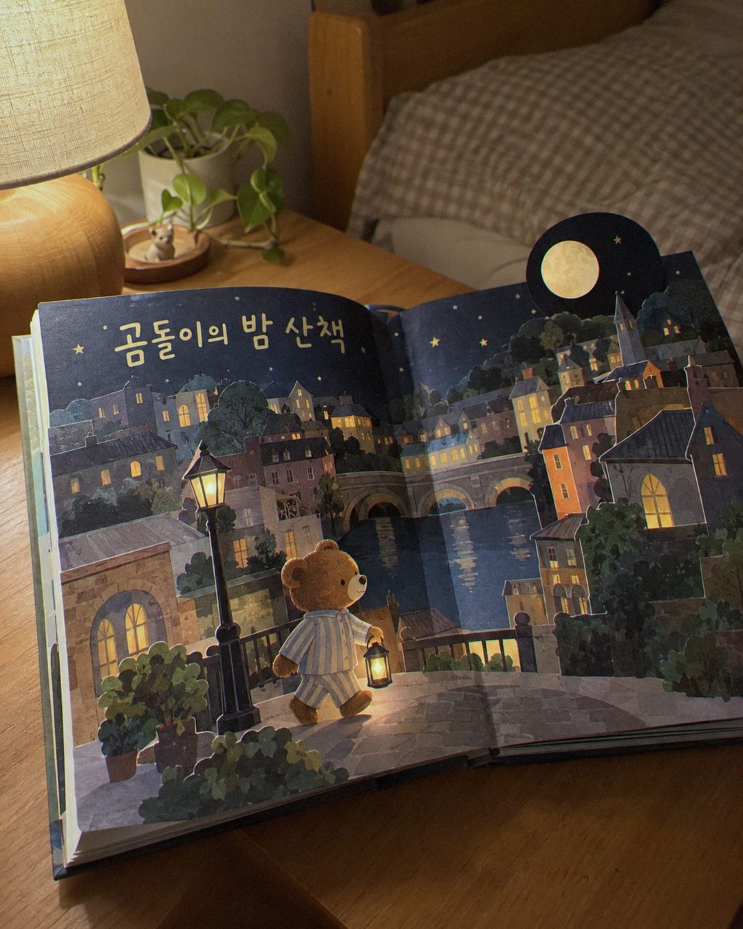 스탠드 불빛 아래 잠옷 입은 곰 캐릭터가 걷는 팝업 그림책 펼침면
